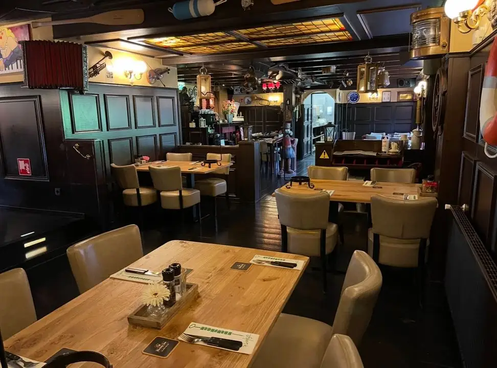 Het restaurant binnen: donker hout, houten tafels en een bar met scheepsattributen