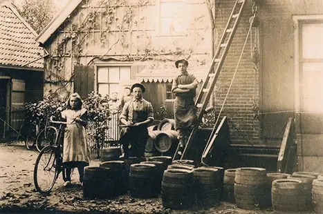 Oude foto van twee mensen bij een boerderij, met een kar en tonnen