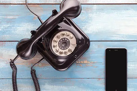 Een oude draaischijftelefoon naast een mobiele telefoon
